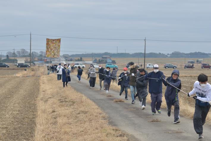 たくさんの人々が大凧の綱を引いて、凧を揚げようとしている