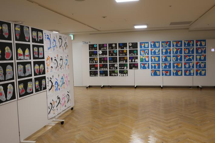 展示スペース左側と正面側それぞれの壁面（ついたてパネル）にたくさんの児童絵が貼付されている様子の画像。
