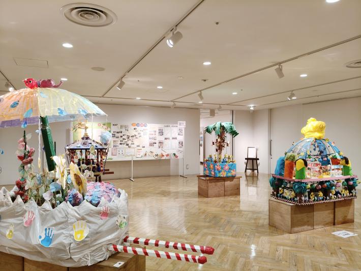 4つの立体作品が展示され、奥の壁に地域子育て支援センターの紹介が展示されている様子