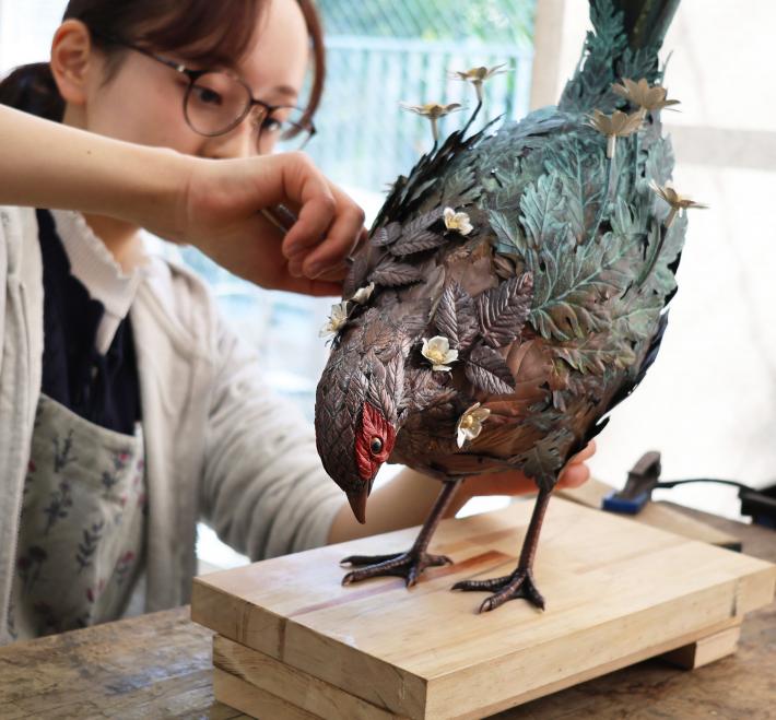 「野に咲く」の制作風景。眼鏡をかけた女性が作品に手をかけている。