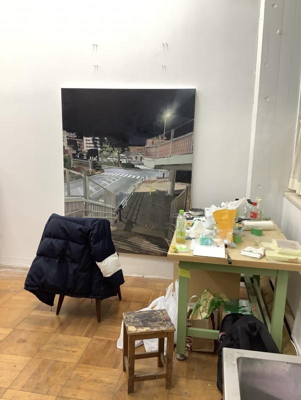 作品の前にジャンパーをかけた椅子と飲み物や画材が載った作業台がある。