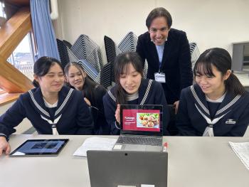 パソコンに向かってイラストを見せて説明する女子生徒たち