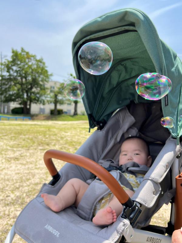 ベビーカーに乗ってシャボン玉を見ている赤ちゃんの写真