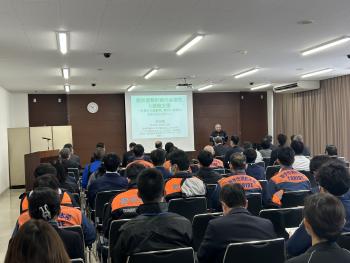 前方スクリーンに映された映像を見る着座の職員たち