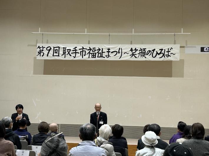 福祉まつりと書かれた看板の下から挨拶をする男性