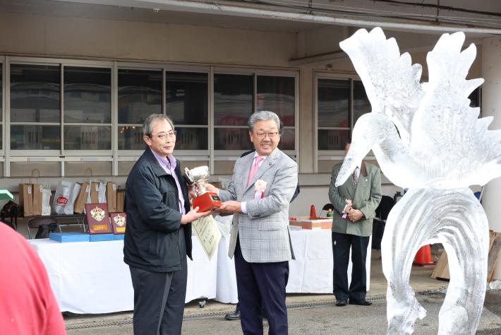 氷彫刻の前で表彰状を渡す男性
