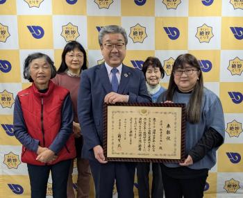 賞状をもってパネルの前に立つ男女