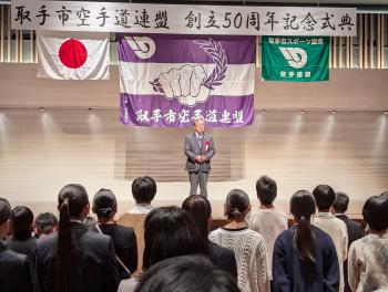 壇上で挨拶をする男性の前で話を聞くこどもたち