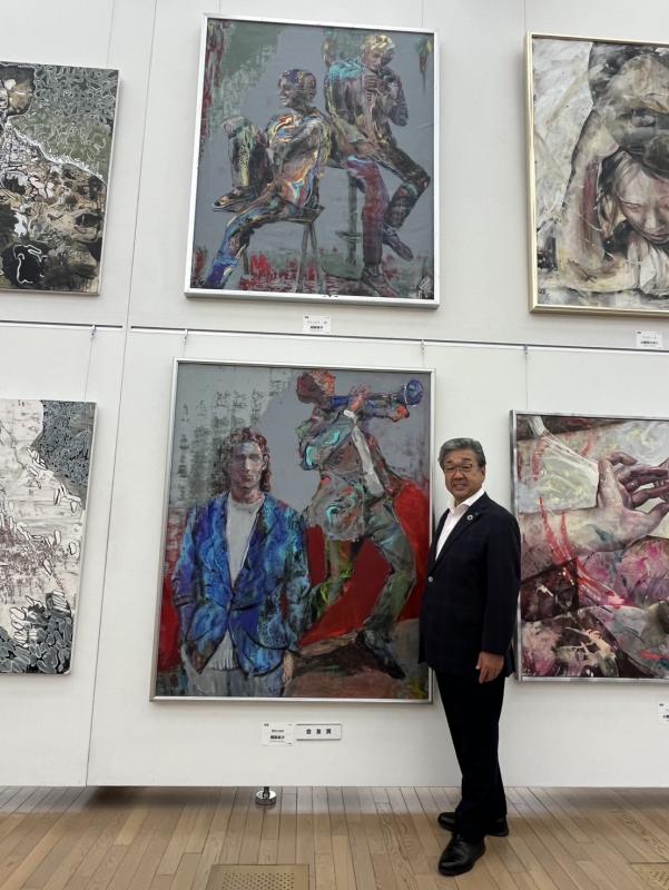 浅岡先生の絵画の隣に立つ男性