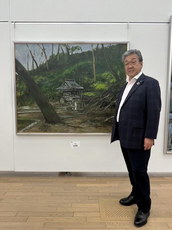 松田先生の絵画の隣に立つ男性