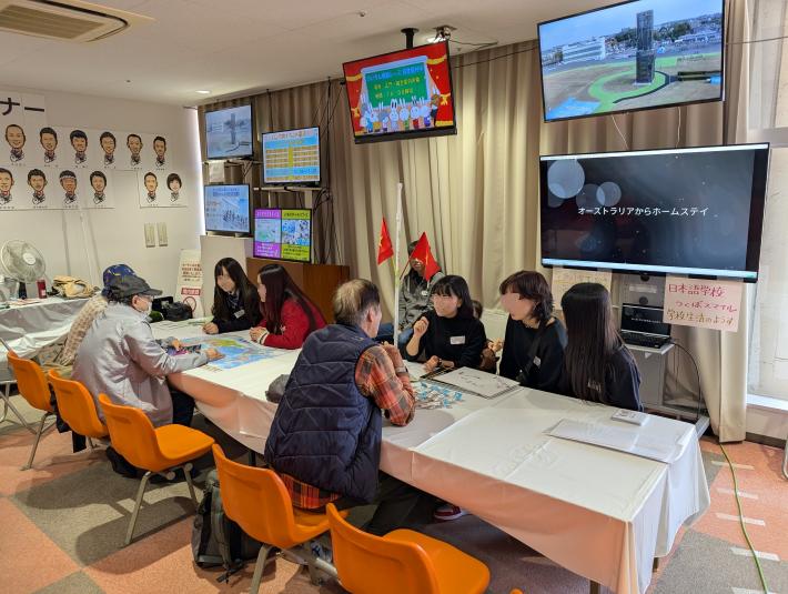 机を囲んで話をする大人と学生