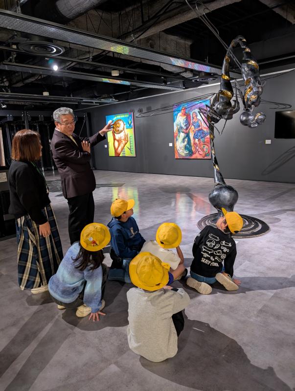 床に座るこどもたちと話をする男性