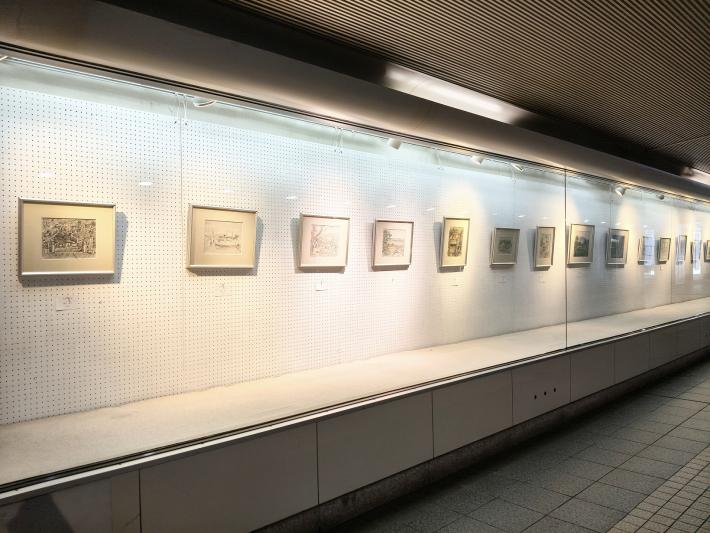 ガラスケース型のギャラリーに複数の絵画作品が飾られている様子