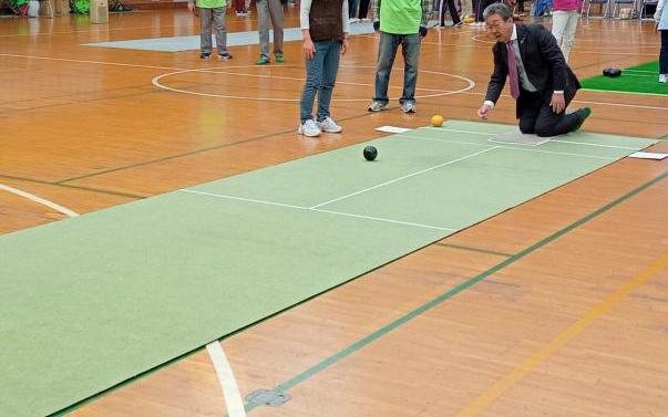 体育館内において、中村市長が床に敷かれたシートの上でボールを転がしている様子