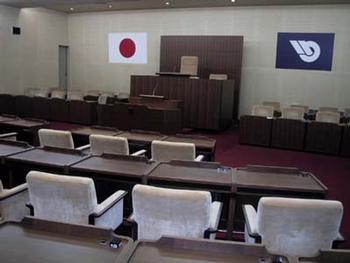 議場の写真画像。議長席が奥にあり壁には日本の国旗と取手市のシンボルマークの旗が飾られている