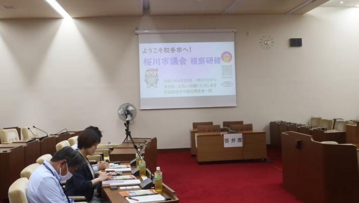議場で男性と女性の職員が座席に座って説明を聞いている