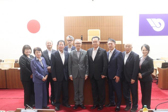 議場で男女数名の議員が立って横に並んでいる