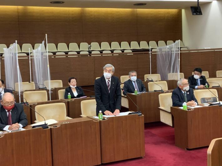 議席に間隔を開けて座る鹿嶋市議。中央の男性(鹿嶋市議会議長)がその場で起立してあいさつをする写真。