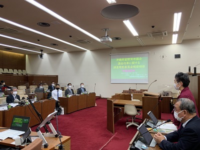 議席に宜野湾市議会の皆さんが座っている。普段職員が座っている前方の席で起立し挨拶をする短髪の女性議員(齋藤議長)