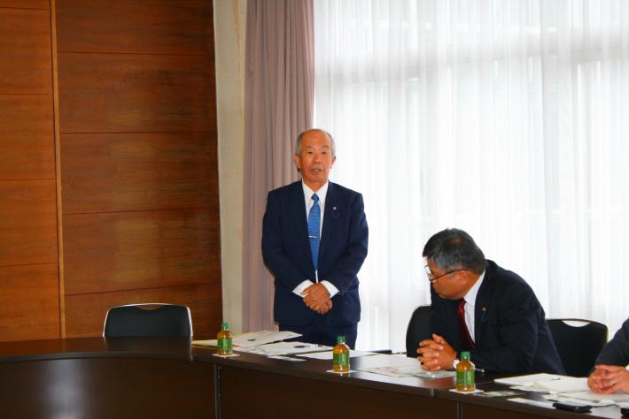 起立して挨拶をする飯田議長と、隣に着席している男性議員の写真。