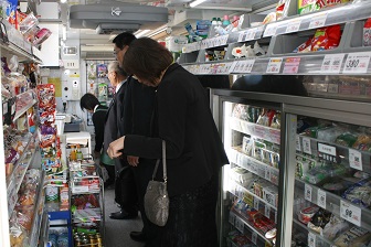 たくさん商品が陳列された棚の間に黒いスーツを着た短髪の男性2人と女性1人が立っている