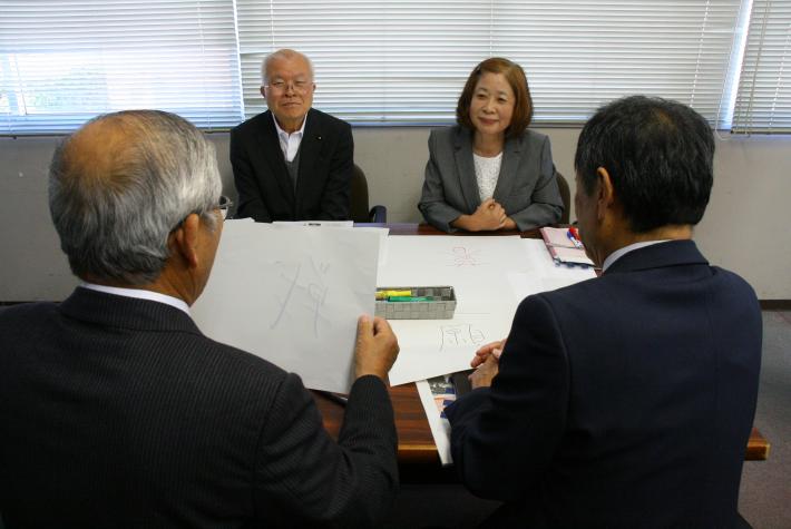 4人で1つのグループになって座っている。1人の男性議員が紙に書いた漢字1文字を他の3人に見せながら自己紹介をしている写真。
