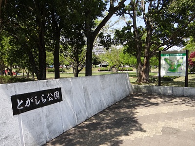 とがしら公園入口。とがしら公園の看板が手前にあり、木々に囲まれた広場が奥に見える。