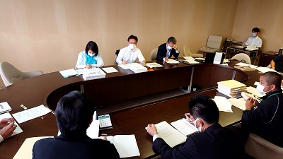 角丸長方形の机に座る男性議員・女性議員と担当課職員。ヒアリングを行っている写真。