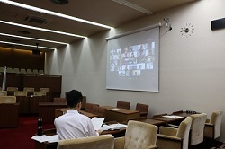 議場スクリーンにオンライン参加している約20人の議員が映っている。