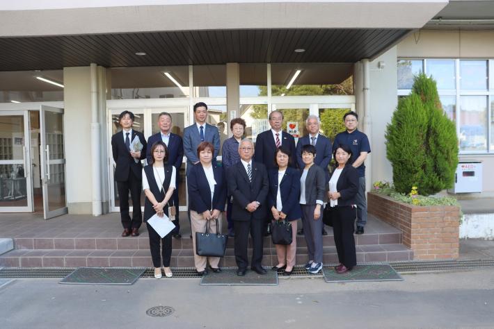 男女の議員十数名が学校の昇降口の前に立っている