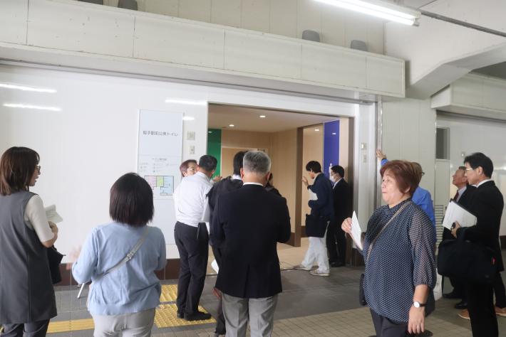 取手駅前公衆トイレの入り口で議員十数名が説明を聞いている