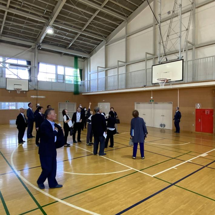 学校の体育館の中で議員十数名がエアコンの設置状況を見ている