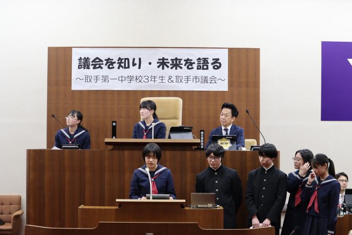 中学生が登壇席と議場席に座って発表している