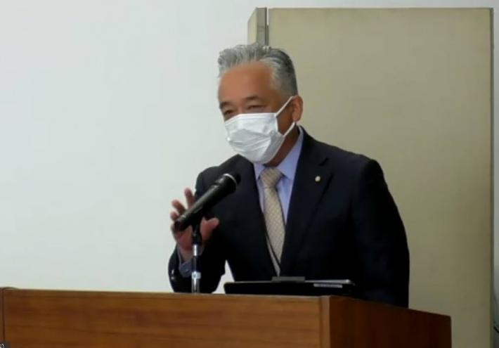 スーツを着た男性議長が壇上で開会のあいさつをしている写真