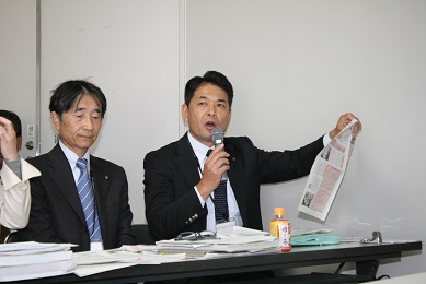 座席に座ったまま議会報を持ち説明をする男性議員(落合総務文教常任委員)