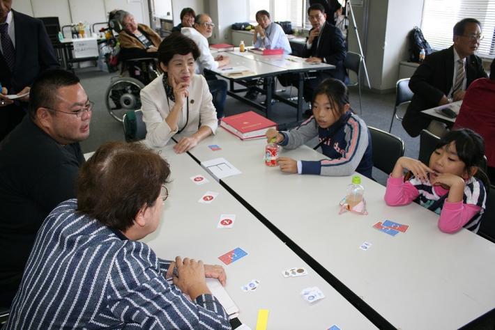 赤い本が机上に置かれた机の周りに参加者が座る。この島には5人が参加。うち2人が女子小学生。