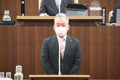 灰色と赤系統のストライプのネクタイを着けた男性議員（金澤議長）が壇上で就任挨拶をしている