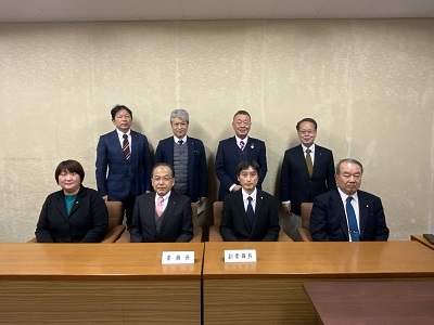 前列に4人が座り、後列に4人が立つ。前列は中央左に男性委員長、中央左に男性副委員長が座る。委員長の左隣りに女性委員が座る。
