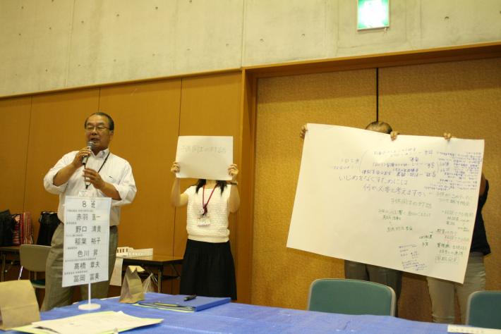 グループ「一般質問」の発表の様子。意見をまとめた模造紙と紙を掲げた参加者の隣で、発表者が話している。