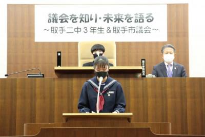 議長候補所信表明演説をする女性生徒(浦野さん)。後ろには男性臨時生徒議長と男性議会事務局長が座る。