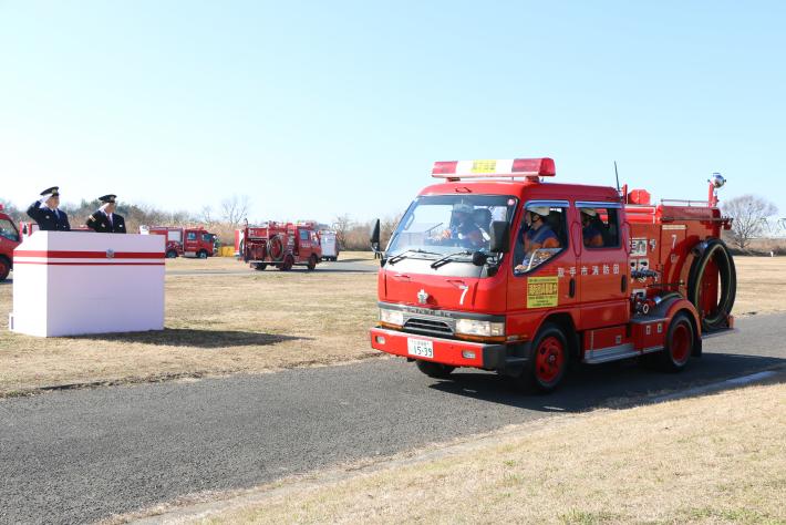 河川敷にて消防車両と消防車両に向かい敬礼する2名の男性