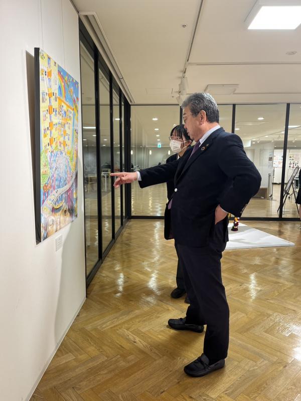 展示された絵画を指を指して見る市長と女性