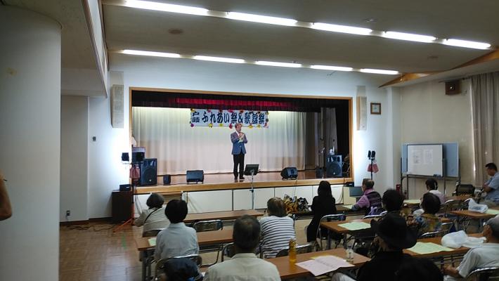 公民館講座室のステージ上でマイクで話をする市長と座っている参加者