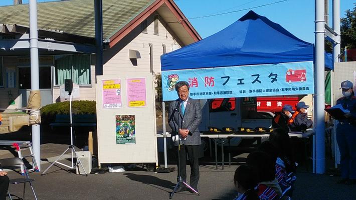 競輪場の外で消防フェスタと書かれた看板の前で挨拶をする市長