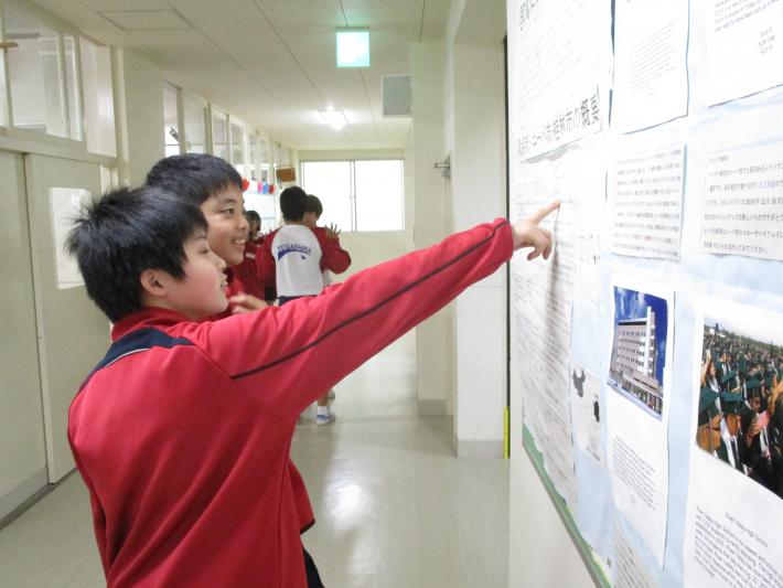 ユーバ市・桂林市の概要が書いてある模造紙を指さしながら見ている戸頭（とがしら）中学校の男子学生2名