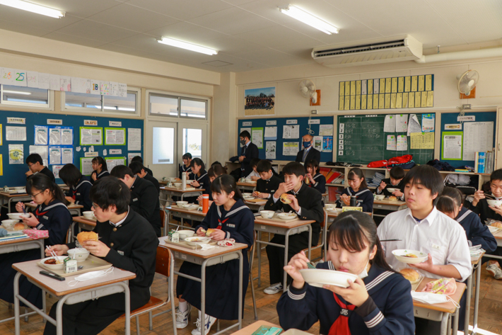 教室内で生徒たちが給食を食べている様子。全員自席に座り、前を向いて食事している。