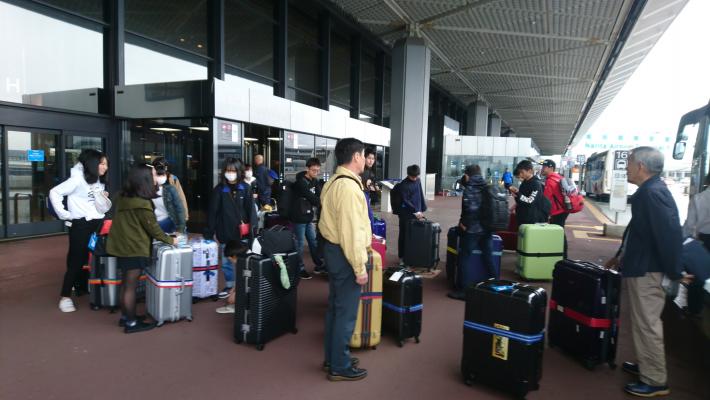 バスの到着口でスーツケースをもって立つ派遣団員