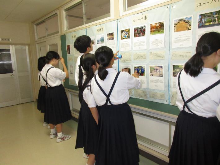 廊下にある壁に掲示されたユーバ市・桂林市学生が作成した作品と、作品を指を指しながら鑑賞する取手第二中学校生