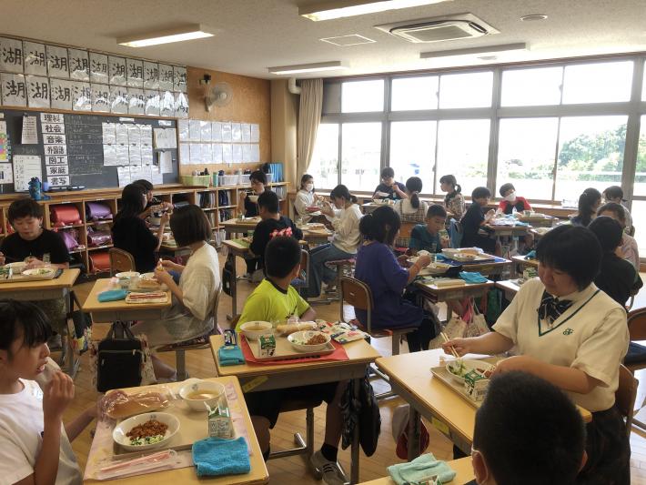 机を囲んで給食を食べる児童と制服を着た生徒