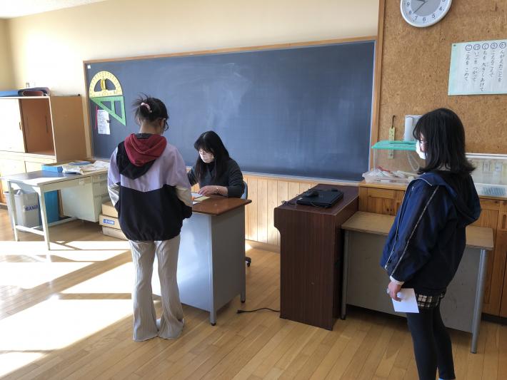 女性教諭が投票の受付をし、投票用紙を交付している。